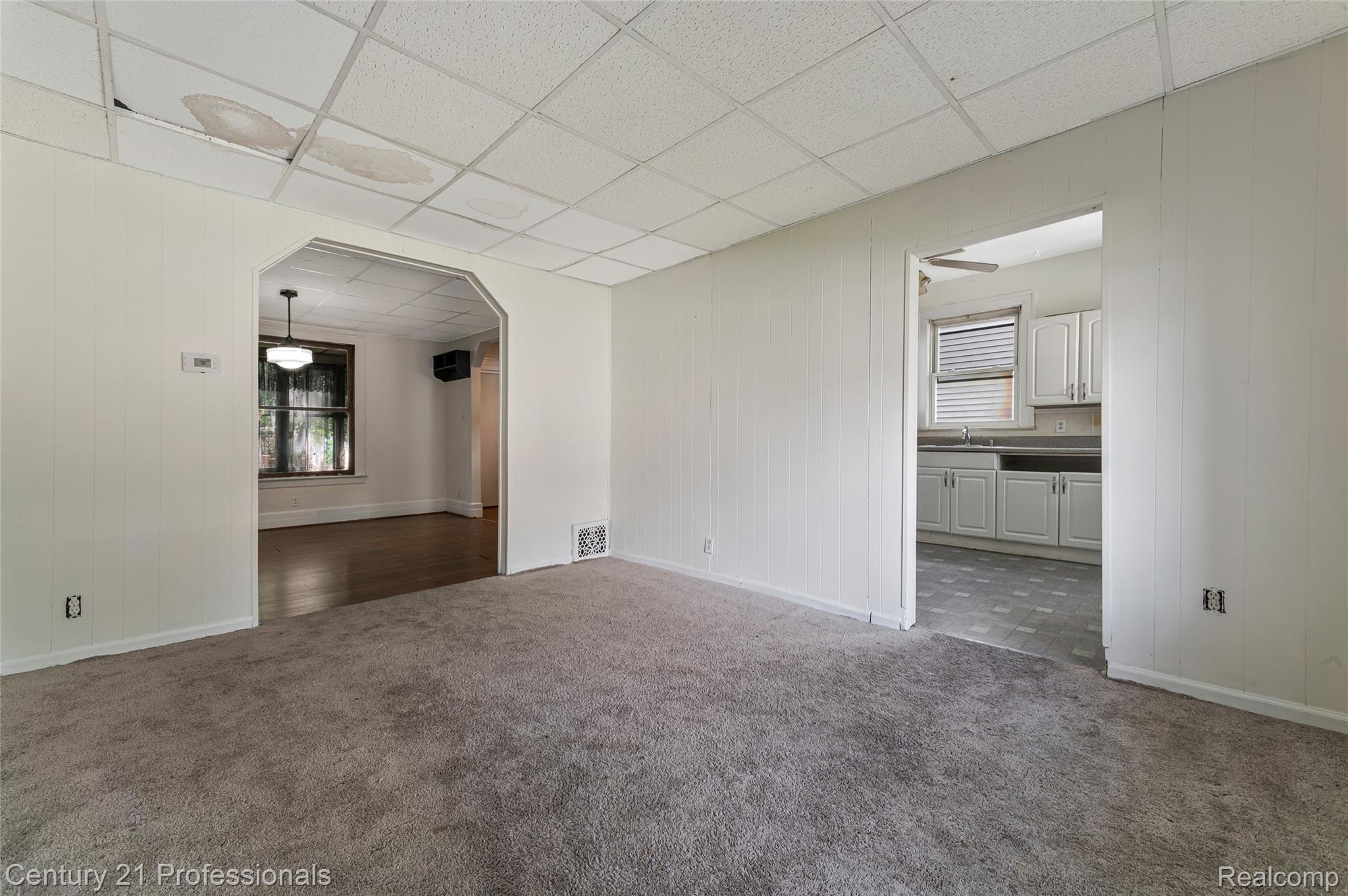 238 Richter Street River Rouge, MI 48218 - Photo 12 of 33 Carpeted room featuring white paneling walls, a tiled ceiling, and open archways leading to rooms with wood-finish flooring and kitchen cabinetry