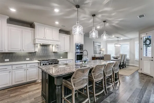 a kitchen with stainless steel appliances granite countertop a stove top oven a refrigerator a sink and white cabinets with wooden floor