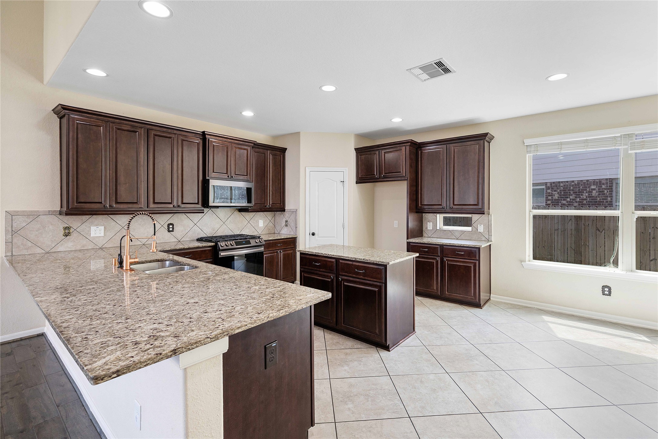 17206 Upper Ridge Lane Humble, TX 77346 - Photo 4 of 50 This kitchen features spacious granite countertops, dark wood cabinets, stainless steel appliances, and a large window for natural light. The open layout is inviting.