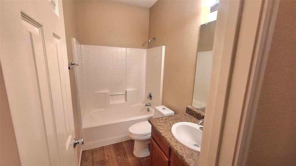 953 Hannah Way Dallas, TX 75253 - Photo 9 of 22 Bathroom featuring a white tub and shower combination with a textured surround, a white toilet, and a vanity with a granular countertop and an integrated sink