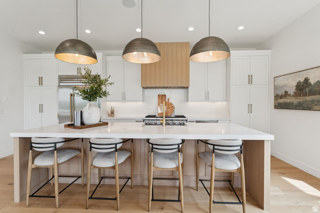1400 Weber Wild Road Oakley, UT 84055 - Photo 11 of 55 Kitchen featuring a large central island with seating, pendant lighting, white cabinetry, integrated stainless steel appliances, and wood-finish flooring