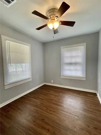 an empty room with wooden floor chandelier fan and windows