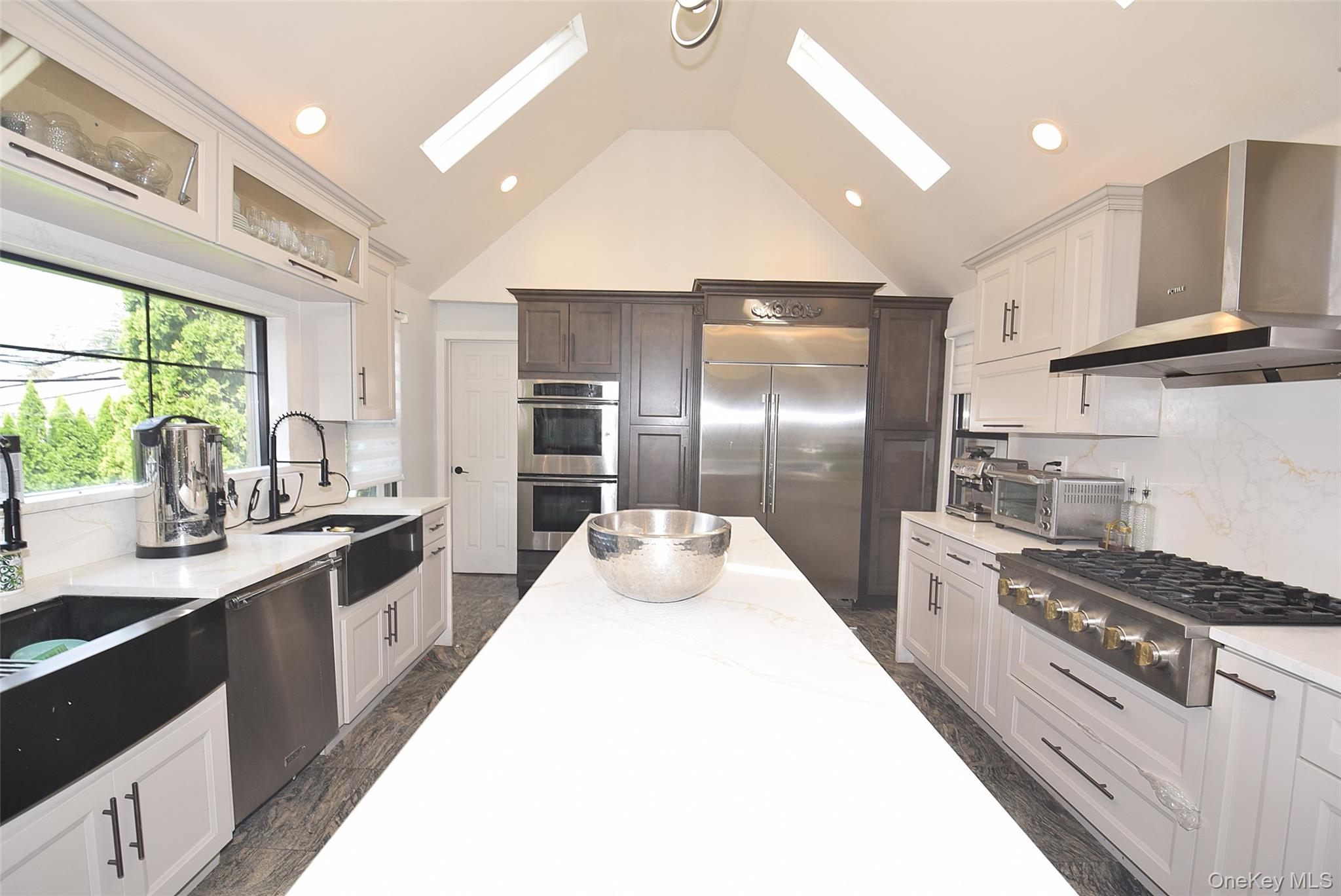 Vaulted ceiling kitchen featuring white cabinetry, a large kitchen island, stainless steel appliances, and skylights