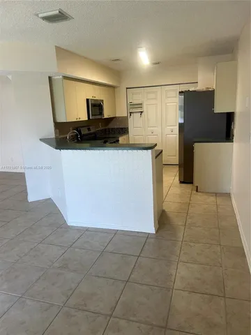a view of a refrigerator in kitchen and an empty room