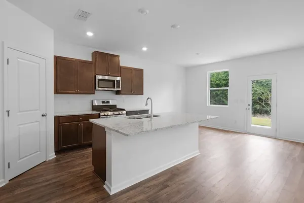 a kitchen with stainless steel appliances granite countertop a stove top oven a sink and a microwave oven on the wooden floor