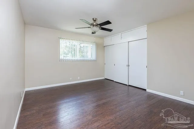 an empty room with wooden floor ceiling fan and windows