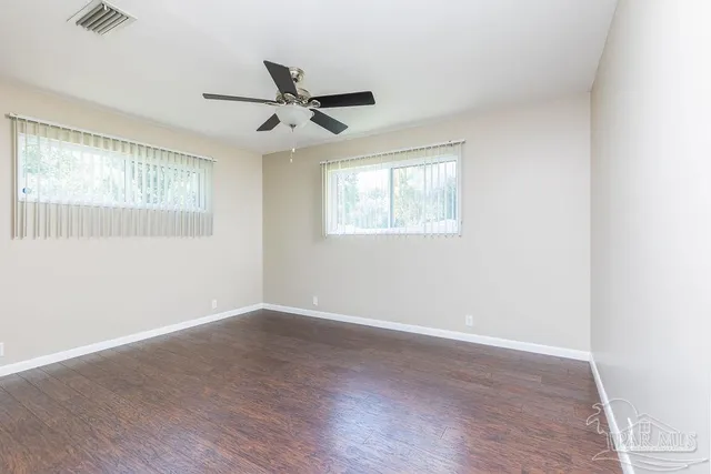 an empty room with wooden floor ceiling fan and windows