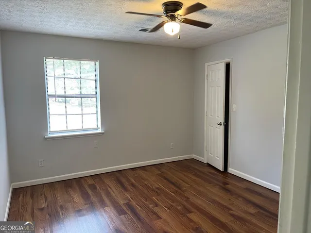 an empty room with wooden floor fan and windows