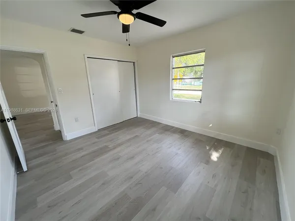 an empty room with wooden floor fan and windows