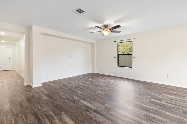an empty room with wooden floor chandelier fan and windows