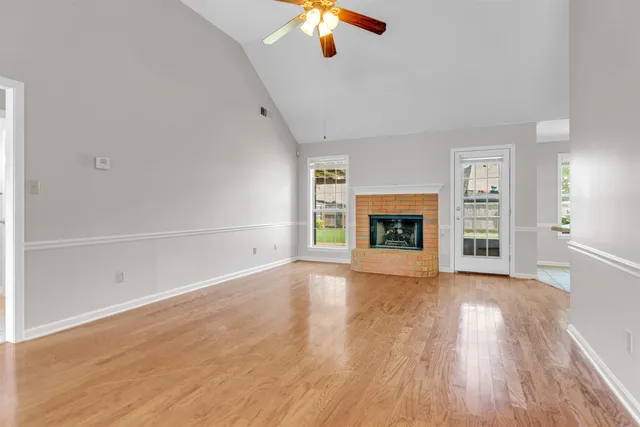 a view of an empty room with wooden floor fireplace and a window