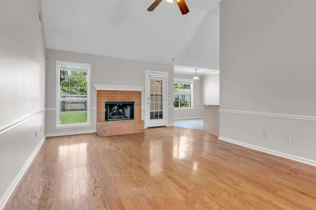 a view of an empty room with wooden floor fireplace and a window