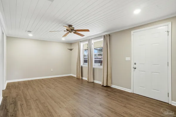 an empty room with wooden floor chandelier fan and windows