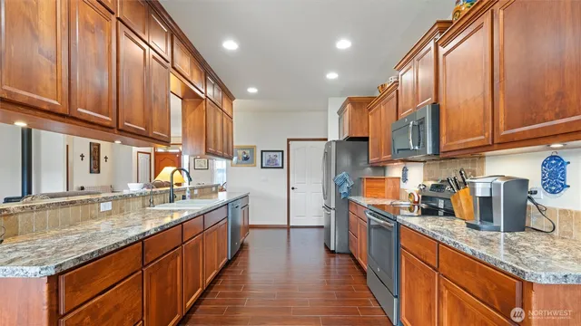 a kitchen with stainless steel appliances granite countertop a sink a stove and a wooden cabinets