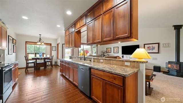 a kitchen with stainless steel appliances granite countertop a sink dishwasher stove and wooden cabinets with wooden floor