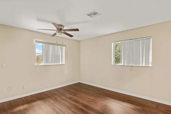 a view of an empty room with wooden floor and a ceiling fan