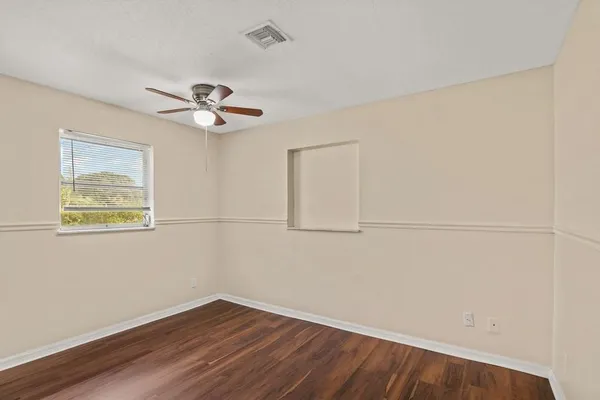 an empty room with wooden floor ceiling fan and window
