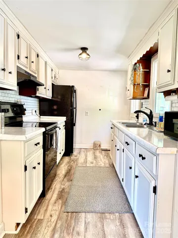 a kitchen with stainless steel appliances a stove top oven a sink a refrigerator white cabinets and wooden floor