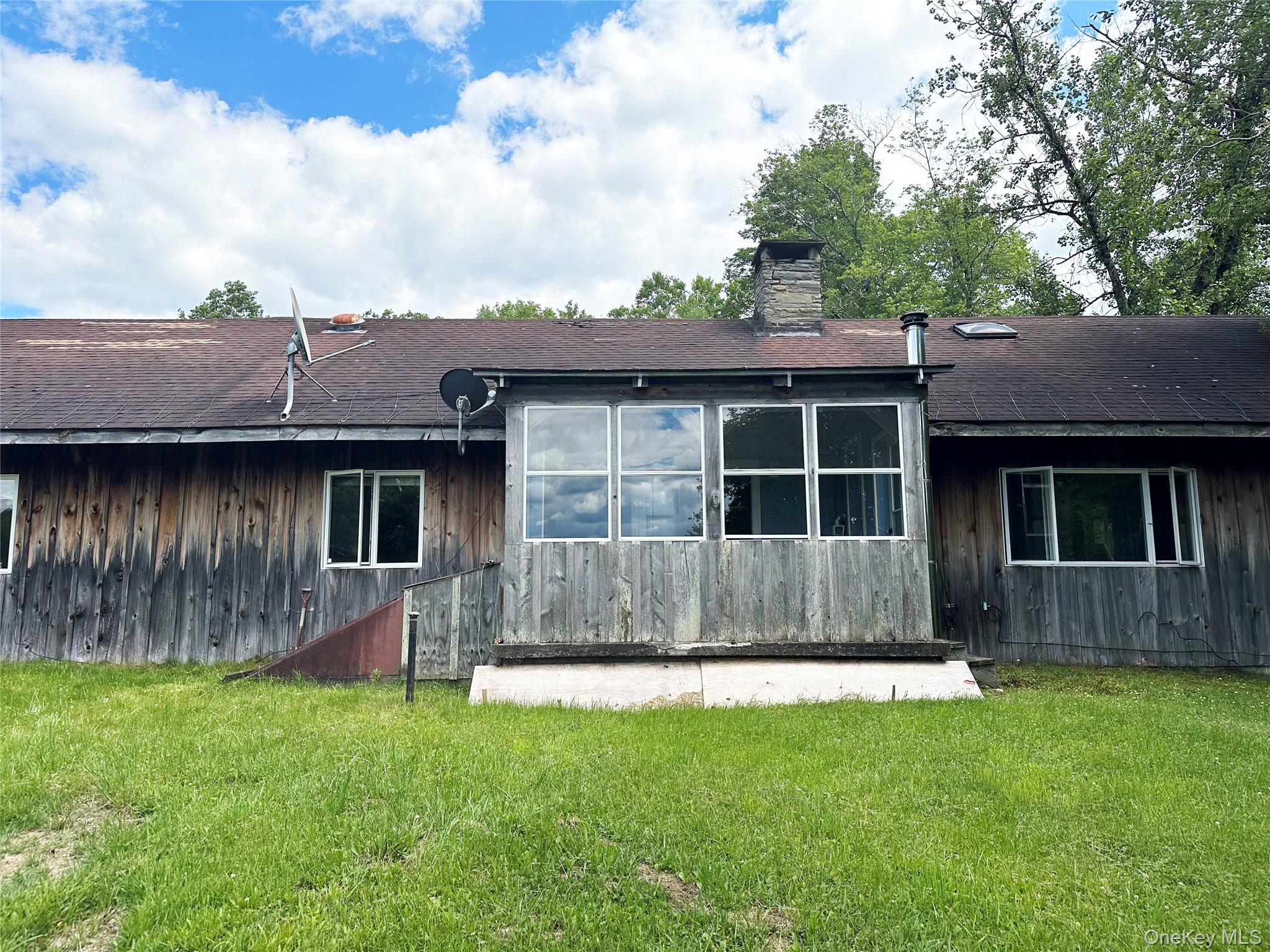 818 Methol Road Roscoe, NY 12776 - Photo 5 of 39 Back exterior of the home with three-season room overlooking the grounds and surrounding greenery, providing additional living space and year-round enjoyment.