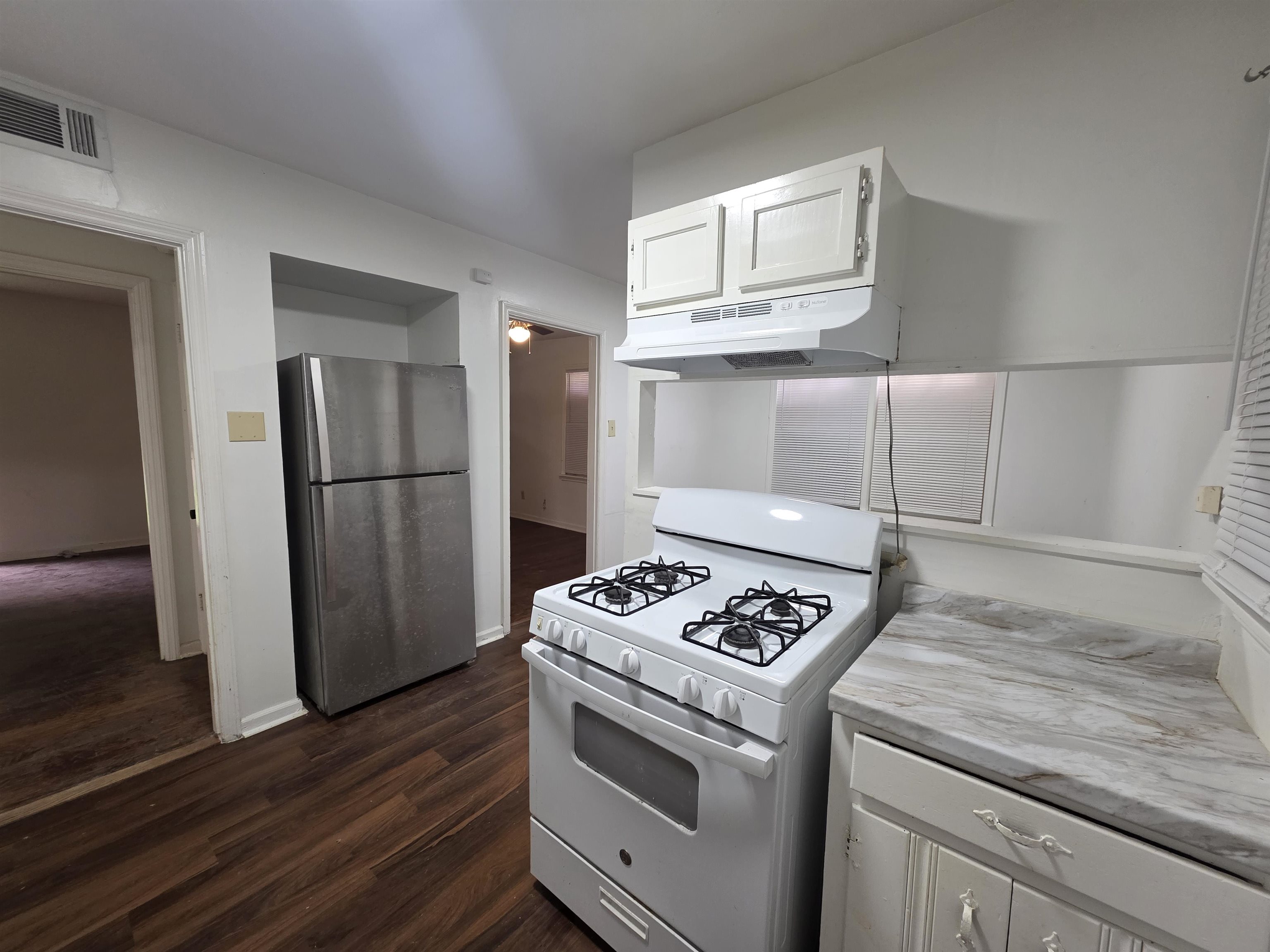 Kitchen featuring wood-finish flooring, white cabinetry, a stainless steel refrigerator, white gas range, and light-toned countertops