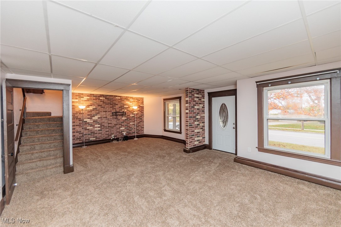3181 Warren Road Cleveland, OH 44111 - Photo 2 of 28 Living Room featuring carpet flooring, a paneled ceiling, and brick wall