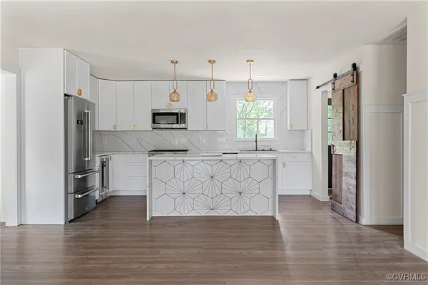 a kitchen with stainless steel appliances granite countertop a refrigerator a stove a sink and white cabinets with wooden floor