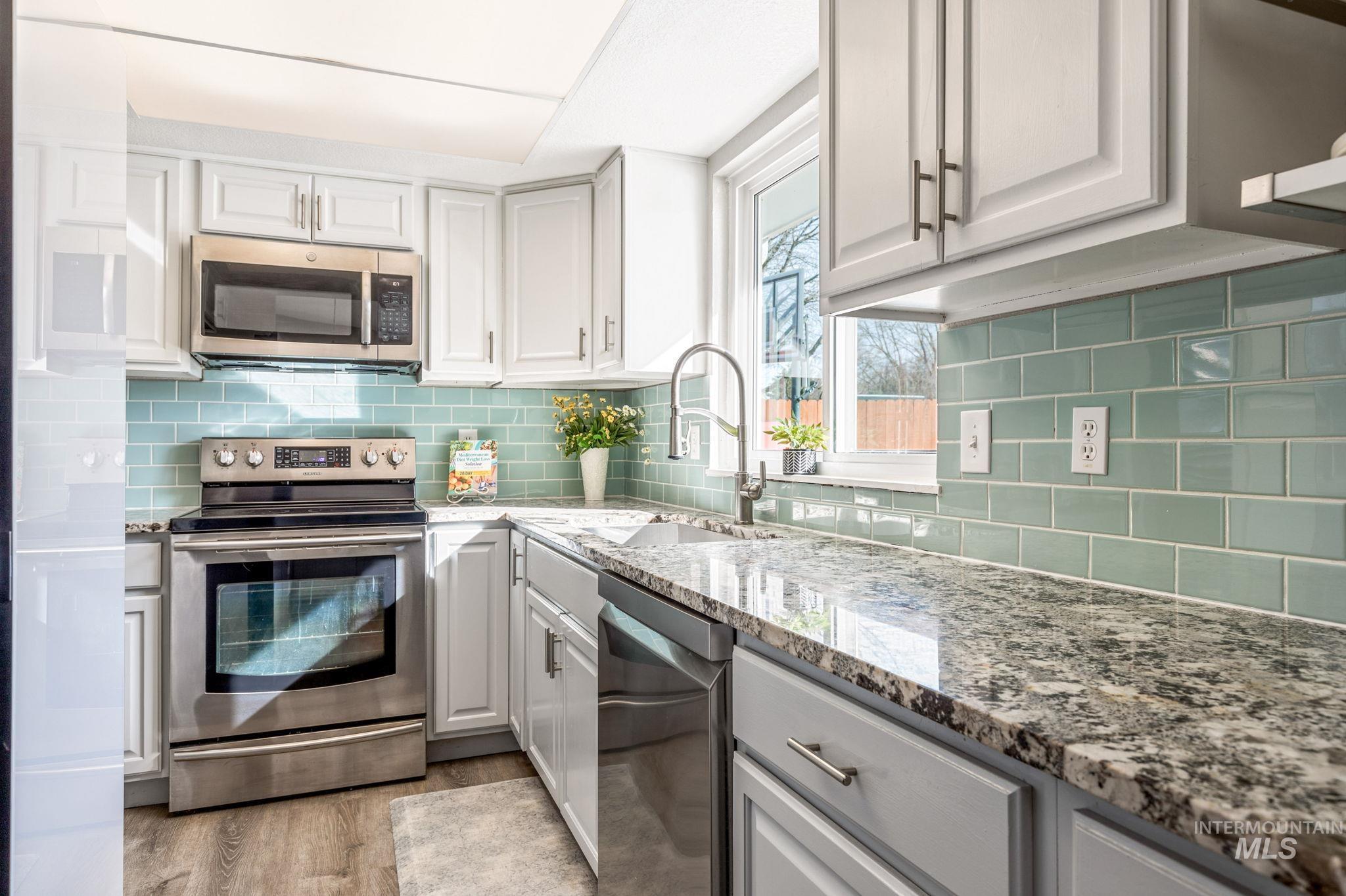 3209 Whitman Drive Boise, ID 83716 - Photo 16 of 45 Kitchen with stainless steel appliances, light stone counters, light wood finished floors, white cabinetry, and tasteful backsplash