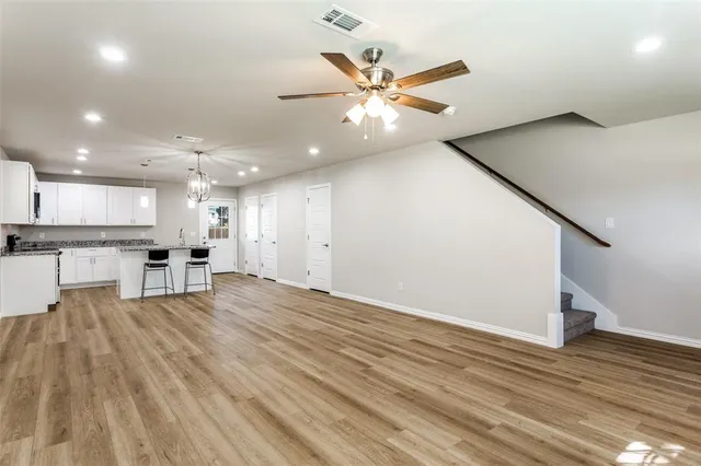 a view of an empty room with wooden floor and a kitchen