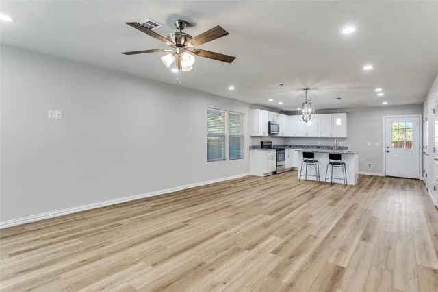 a view of an empty room and kitchen with wooden floor