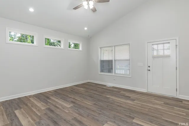 an empty room with wooden floor chandelier fan and windows