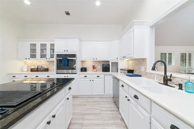 a kitchen with stainless steel appliances white cabinets a sink dishwasher a stove top oven a refrigerator with white cabinets and wooden floor