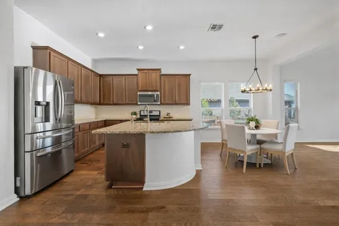 a kitchen with stainless steel appliances granite countertop a refrigerator a stove a sink dishwasher and a dining table with wooden floor