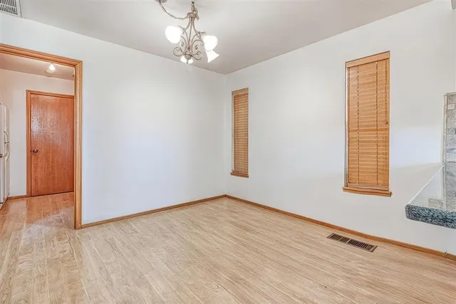 an empty room with wooden floor chandelier and windows