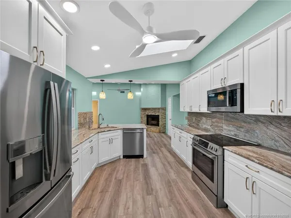 a large kitchen with stainless steel appliances granite countertop a stove a sink dishwasher a refrigerator and a microwave oven with wooden floor
