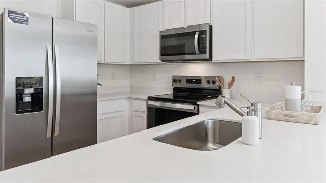 a kitchen with stainless steel appliances granite countertop a refrigerator a microwave a sink and white cabinets