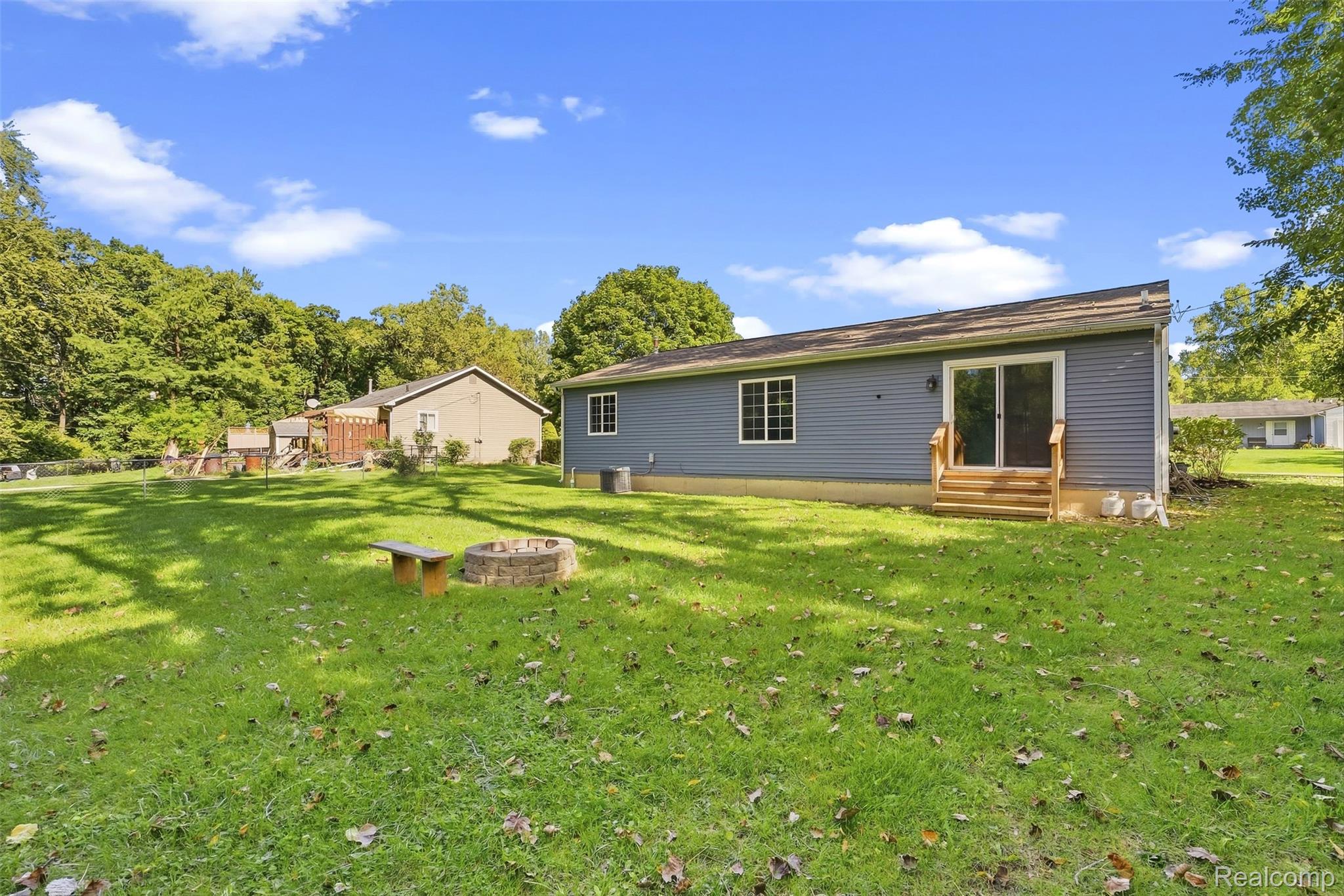 1750 Henbert Road West Bloomfield, MI 48324 - Photo 29 of 32 Expansive grassy yard featuring a stone fire pit and a wooden bench