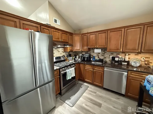 a kitchen with stainless steel appliances granite countertop a refrigerator a stove and a sink with wooden floor