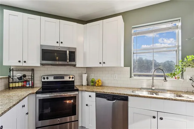 a kitchen with stainless steel appliances granite countertop white cabinets a stove a sink and a microwave