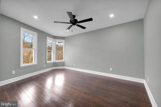 an empty room with wooden floor fan and windows