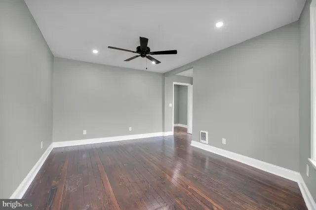 a view of an empty room with wooden floor and a ceiling fan