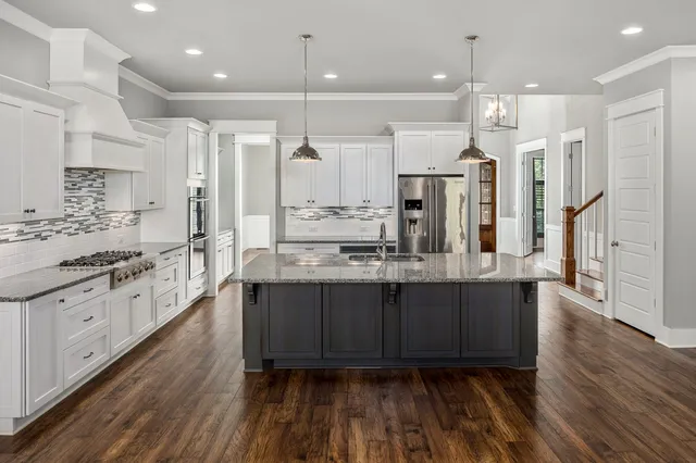 a large kitchen with stainless steel appliances kitchen island granite countertop a large island a stove a refrigerator white cabinets and wooden floor