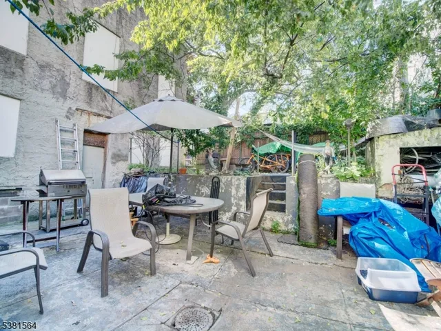 a view of a patio with table and chairs under an umbrella with large trees