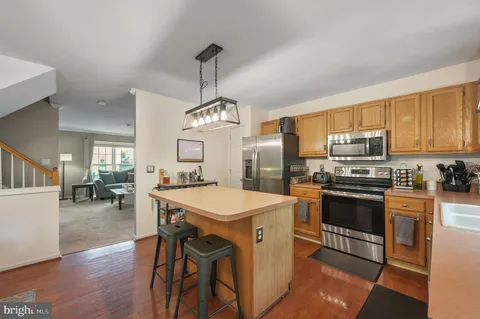 a kitchen with stainless steel appliances a stove a sink dishwasher a refrigerator and a dining table with wooden floor