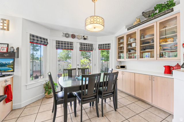 31 Village Square Road Centerville, UT 84014 - Photo 13 of 29 Dining area featuring a bay window with multiple panes, a neutral tile floor, a decorative ceiling light fixture, built-in lower cabinets with a light countertop, and upper cabinets with glass-front doors