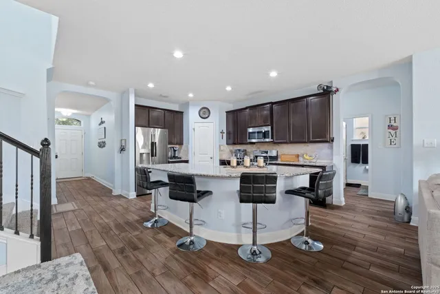 a kitchen with stainless steel appliances kitchen island granite countertop a table chairs refrigerator and microwave