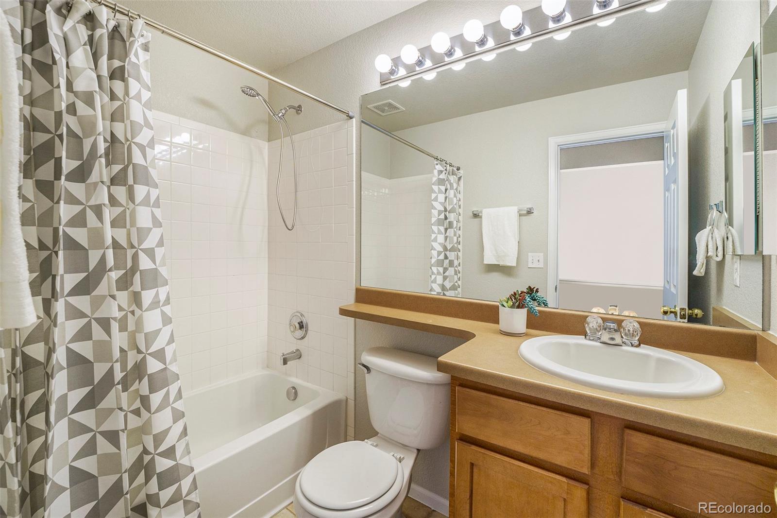 4623 Flower Street Wheat Ridge, CO 80033 - Photo 14 of 23 a bathroom with a sink a toilet a mirror a bathtub and shower