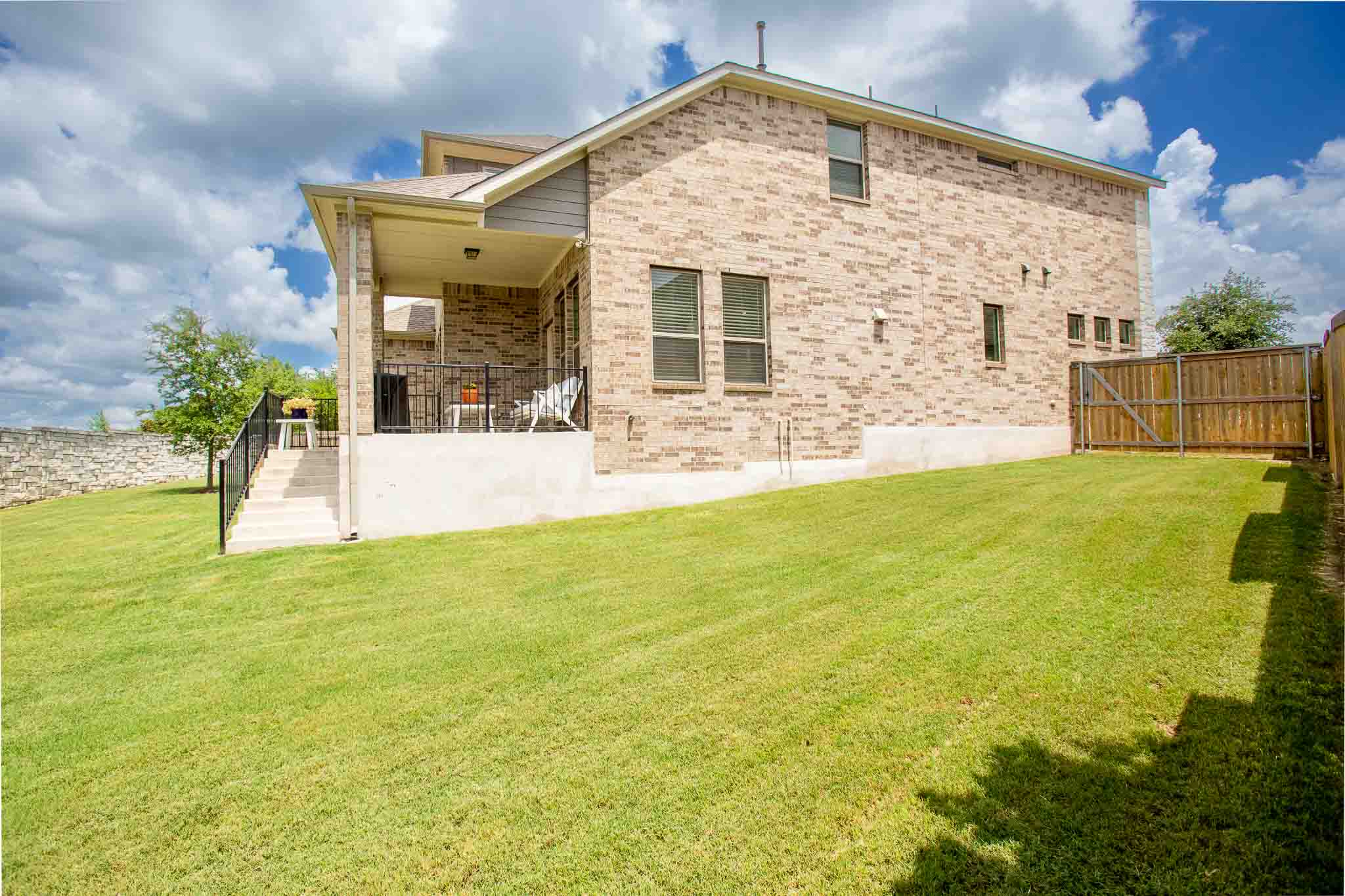 166 West Branch Road Kyle, TX 78640 - Photo 36 of 39 A manicured lawn extends to a brick-clad home with a covered patio and sturdy privacy fence.
