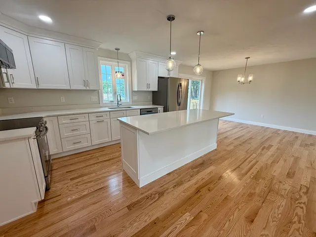 a large kitchen with stainless steel appliances a refrigerator a stove a sink dishwasher a oven and white cabinets with wooden floor