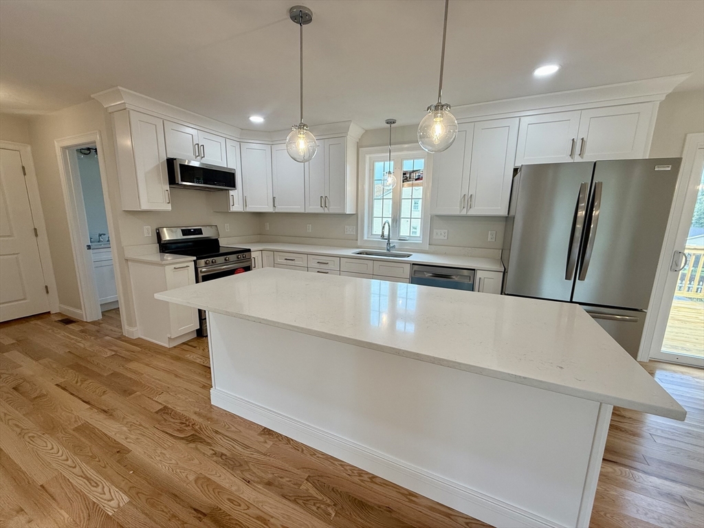 70 Oswego Street Bellingham, MA 02019 - Photo 14 of 28 a large kitchen with stainless steel appliances a refrigerator a stove a sink dishwasher a oven and white cabinets with wooden floor