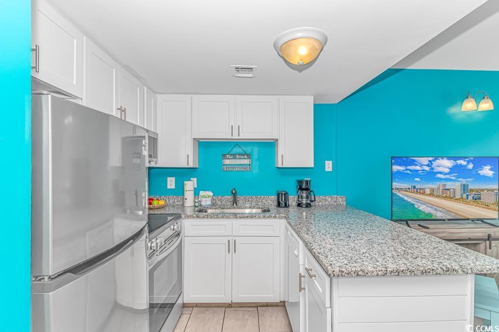 1605 South Ocean Boulevard, Unit 705 Myrtle Beach, SC 29577 - Photo 14 of 38 Kitchen featuring appliances with stainless steel finishes, white cabinetry, light stone countertops, a peninsula, and light tile patterned floors